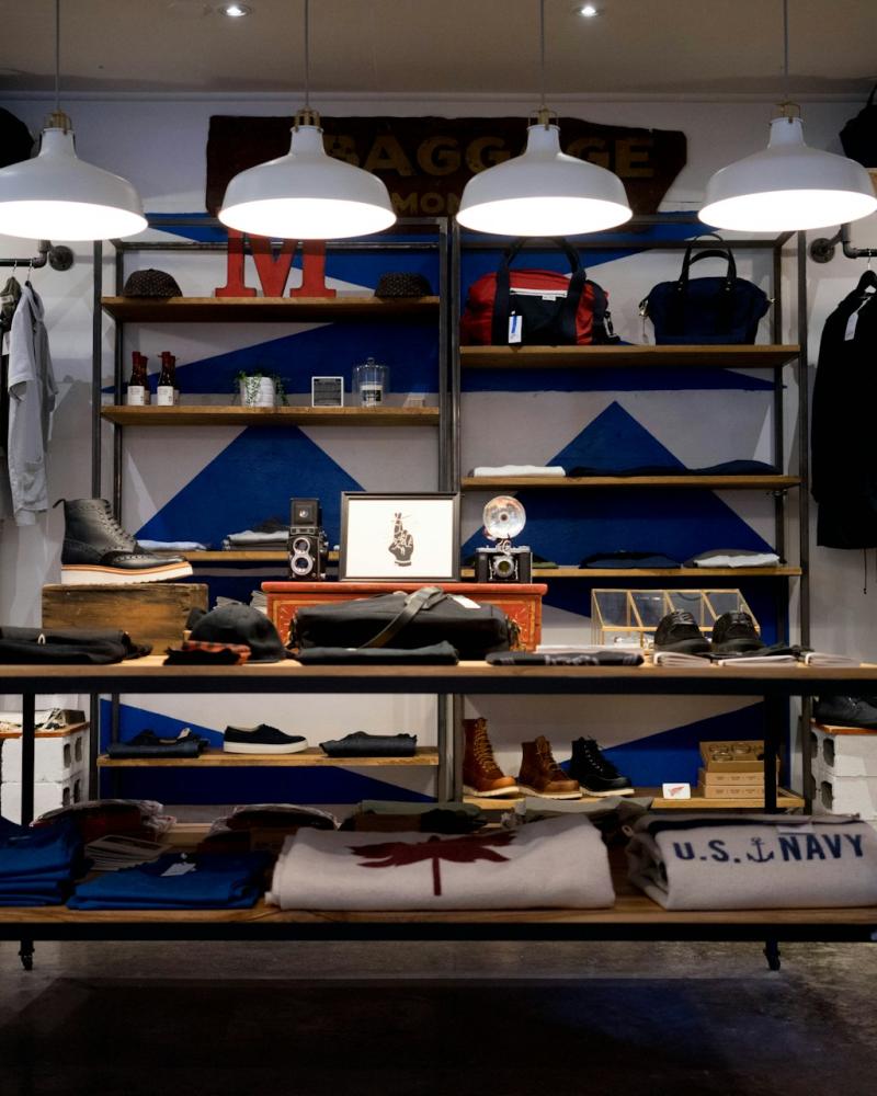 A retail shop interior with shelves displaying bags, accessories, and merchandise under bright hanging lights.